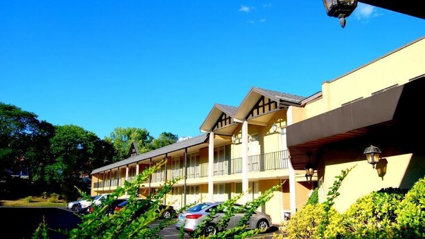 A motel with a two-story structure, a covered parking area, and a clear blue sky.