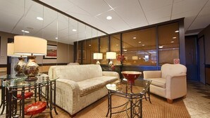 A hotel lobby with a sofa, armchairs, a glass table, and lamps.