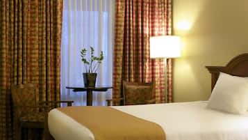 Habitación de hotel con una cama, dos sillas, una mesita con una planta y una lámpara.