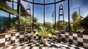 A checkered floor, a potted plant, and two metal ladders in a room with large windows.