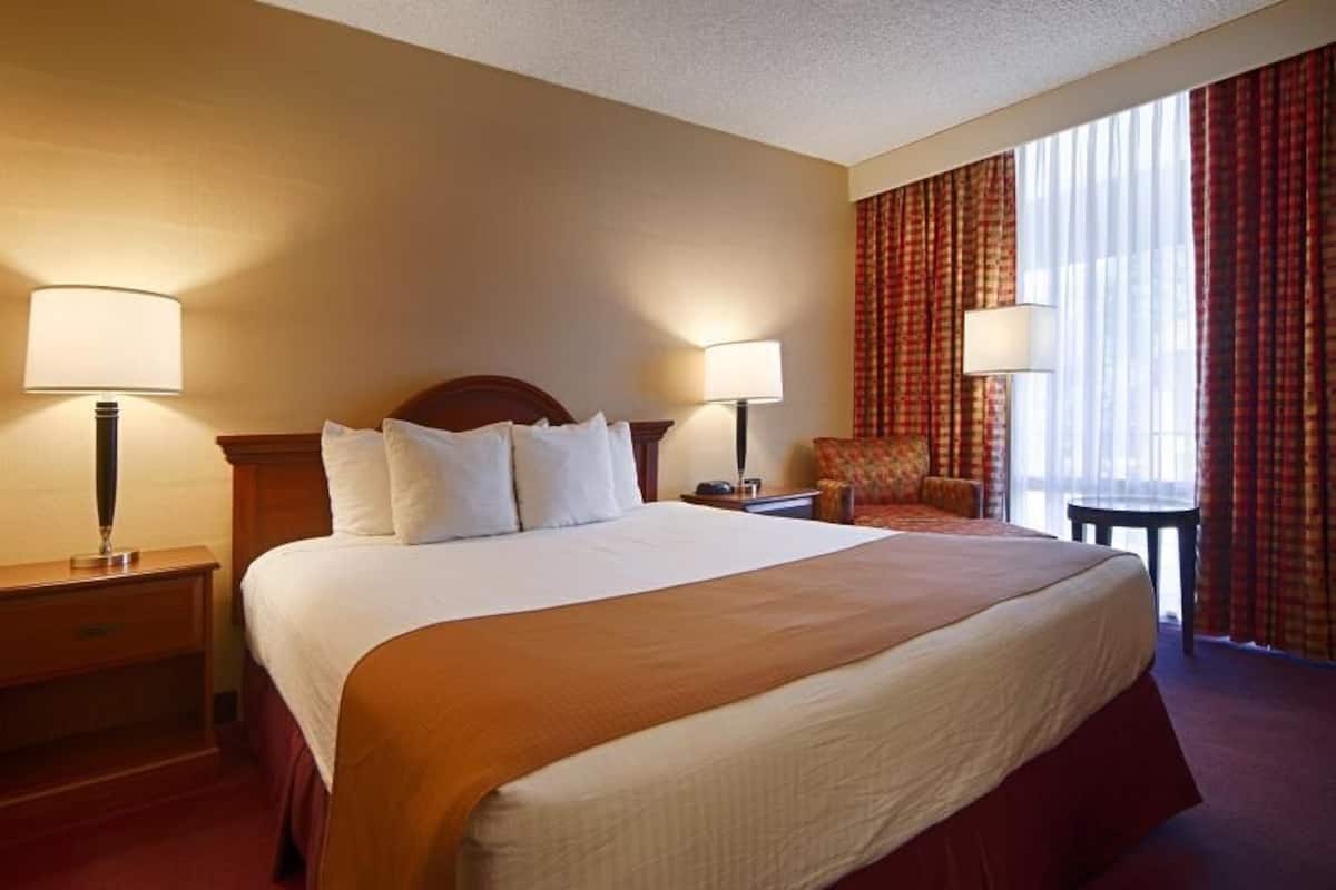 A hotel room with a large bed, two bedside tables with lamps, a chair, and a window with curtains.