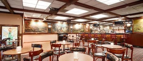 Un restaurante con mesas y sillas redondas, una zona de bar y obras de arte en las paredes.