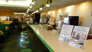 A restaurant with a counter, stools, and a menu board.