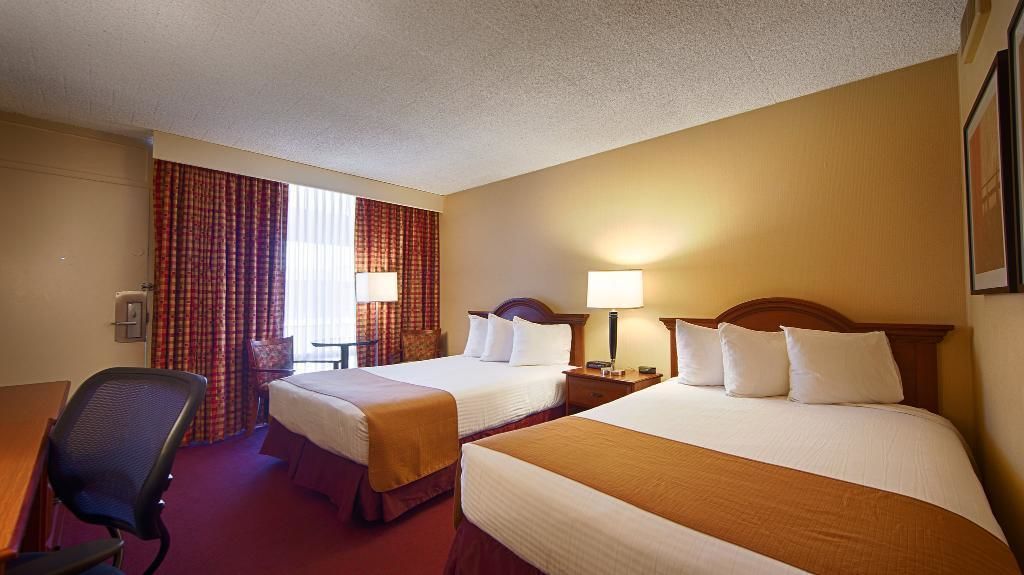 A hotel room with two beds, a desk, a chair, and a window with curtains.