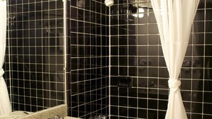 A bathroom with a granite sink, a mirror, a shower with a white curtain, and black tiled walls.