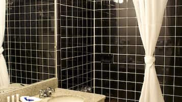 A bathroom with a granite sink, a mirror, a shower with a white curtain, and black tiled walls.