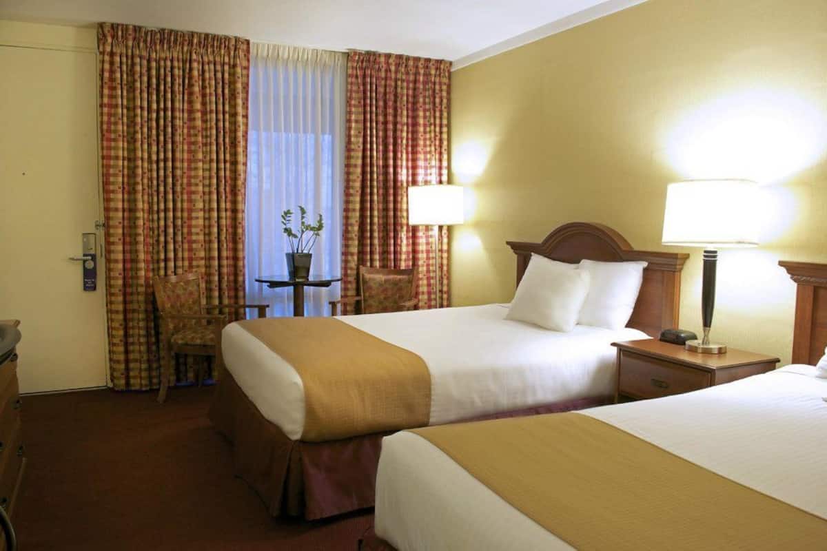 A hotel room with two beds, a desk, a chair, and a window with curtains.