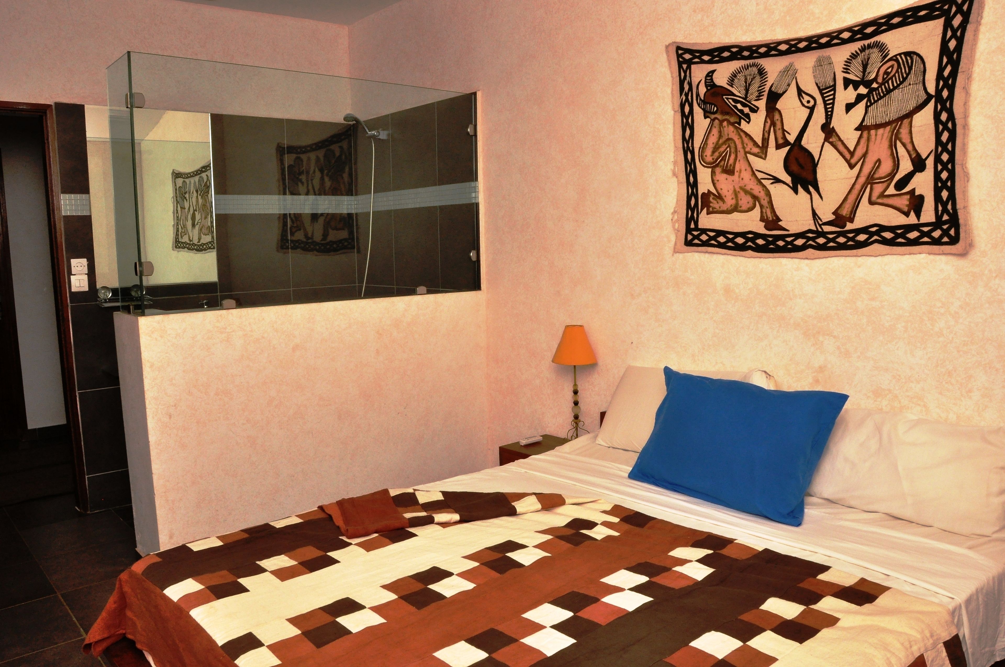 A bedroom with a bed, a nightstand, a lamp, a glass shower enclosure, and a wall painting.