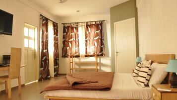 A bedroom with a bed, bedside tables, a desk, a chair, a ceiling fan, and curtains.