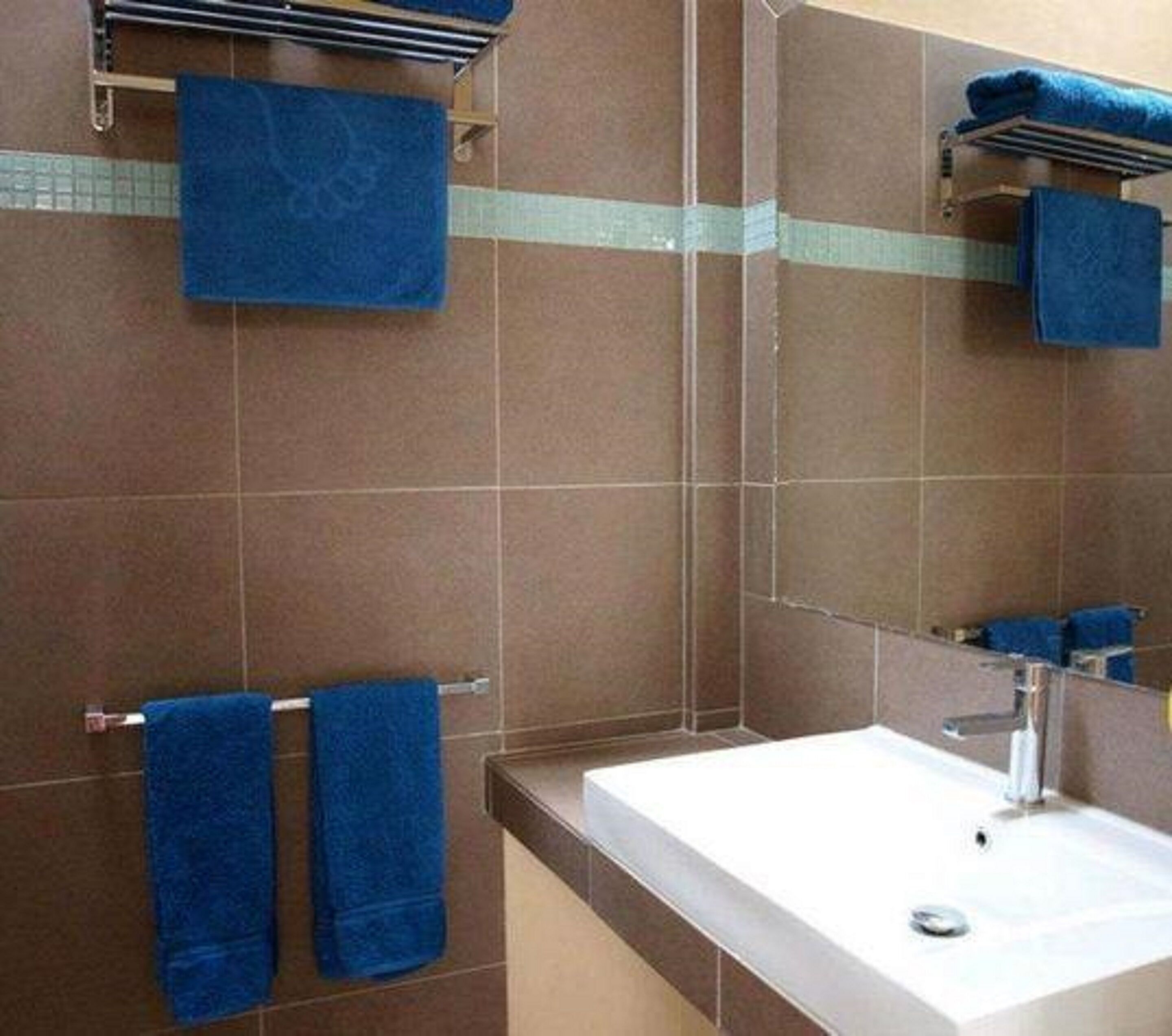 A bathroom with brown tiled walls, a white sink, and two blue towels hanging on towel racks.