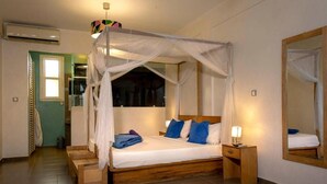 A bedroom with a four-poster bed, a bedside table with a lamp, and a large mirror on the wall. - Casa Mara Guest House (Dakar)