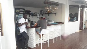 A bar area with a counter, stools, and a variety of bottles and glasses on shelves. - Casa Mara Guest House (Dakar)