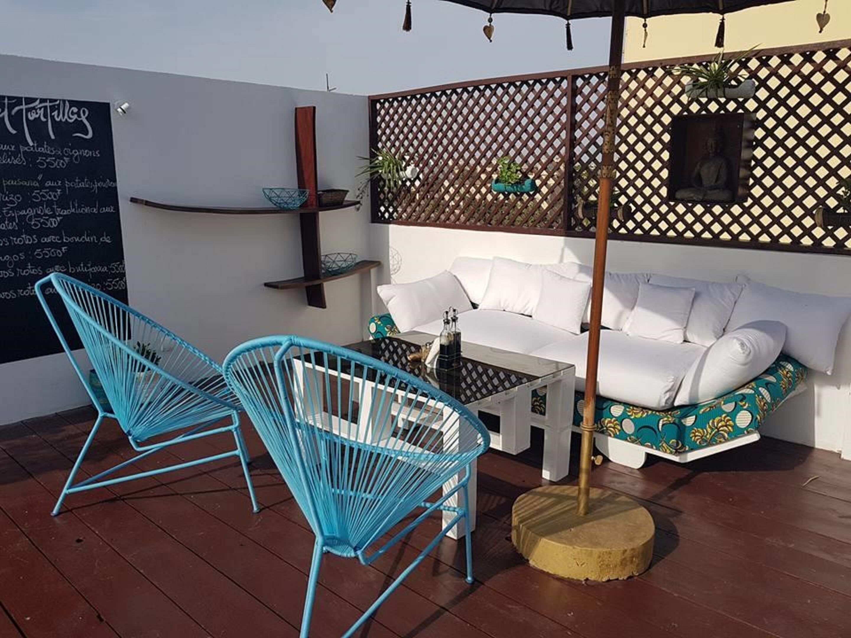 A cozy outdoor seating area with a white sofa, two blue chairs, a small table, and a decorative fence.