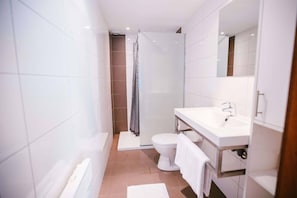 Un baño moderno con azulejos blancos, un lavamanos blanco, un inodoro y una zona de ducha.