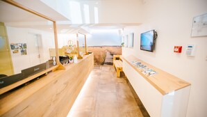 A modern, well-lit reception area with wooden counters, a digital screen, and a pathway leading to a beach view. - Le Val D'Arimont Resort (Malmedy)