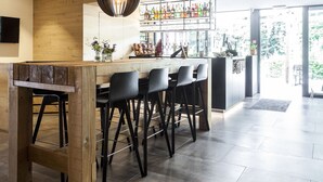 A modern kitchen with a bar area, featuring a wooden bar counter, black bar stools, and a hanging pendant light. - Le Val D'Arimont Resort (Malmedy)