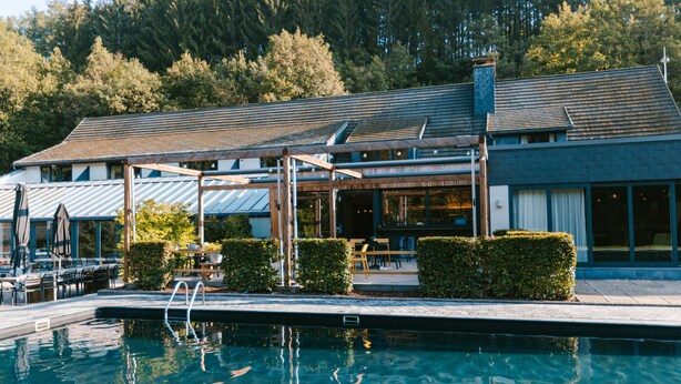 A modern hotel with a swimming pool, outdoor seating, and a covered patio area. - Le Val D'Arimont Resort (Malmedy)