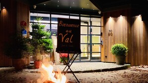 A fire pit with a welcome sign in front of a building with wooden walls and a glass entrance. - Le Val D'Arimont Resort (Malmedy)