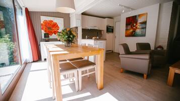 A modern living room with a wooden dining table, a sofa, and a kitchen in the background.