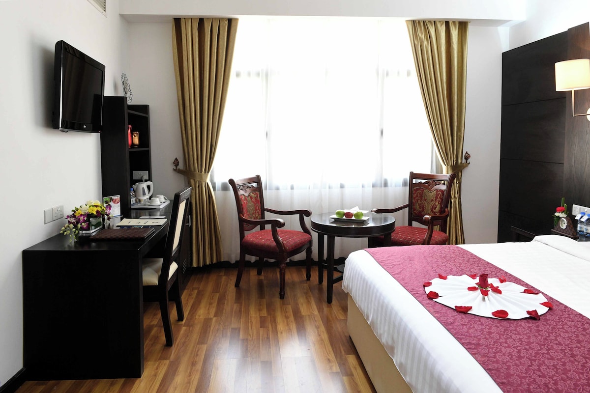 A hotel room with a bed, a desk, a chair, a small table, and a television.