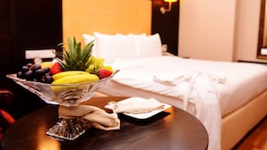 A hotel room with a bed, a bedside table with a fruit bowl, and a nightstand with a lamp. - JUFFAIR GATE HOTEL (Manama)