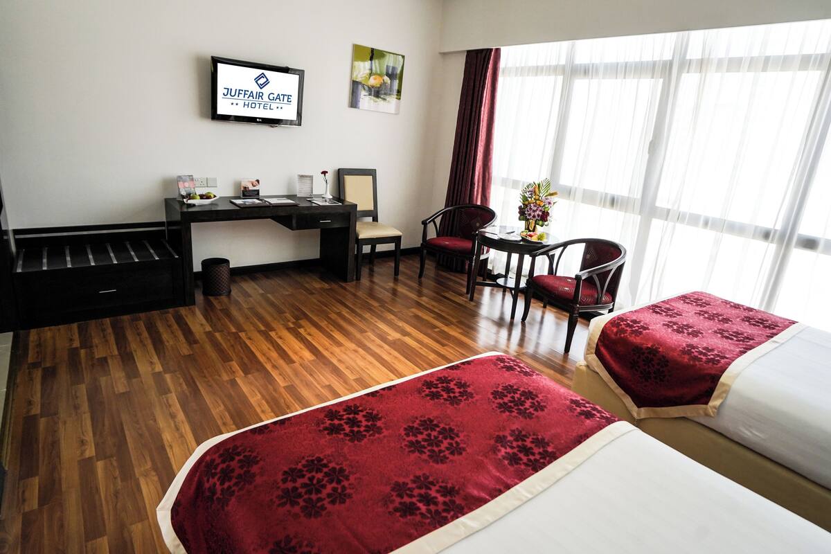 Habitación de hotel con dos camas, un escritorio, una silla, un televisor y una ventana con cortinas.