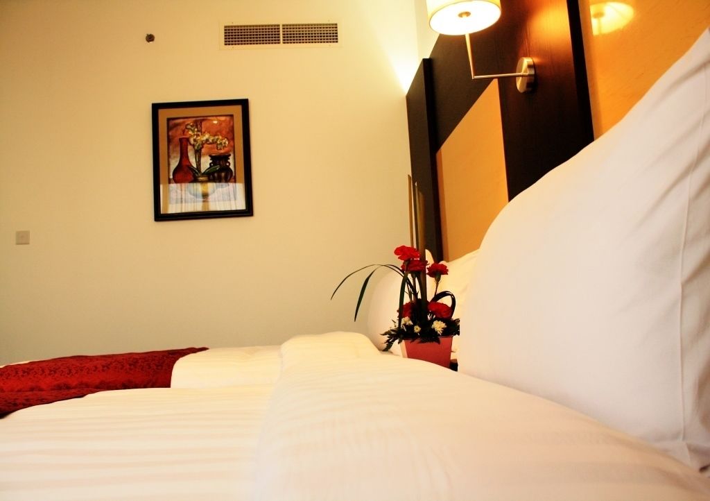 Una habitación de hotel con una cama, una obra de arte enmarcada en la pared y una mesita de noche con un florero.