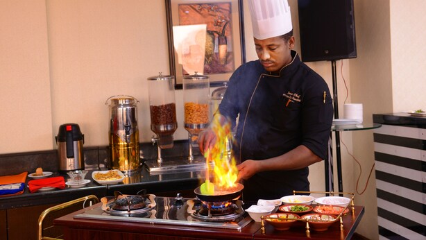 A chef cooking with flames on a stove in a kitchen setting. - JUFFAIR GATE HOTEL (Manama)