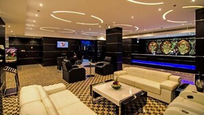 A modern lounge area with a checkered floor, leather sofas, a flat-screen TV, and a decorative wall with circular light fixtures. - JUFFAIR GATE HOTEL (Manama)