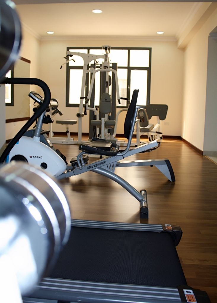A gym with exercise equipment, including a treadmill and weight machines, in a room with wooden flooring and large windows.