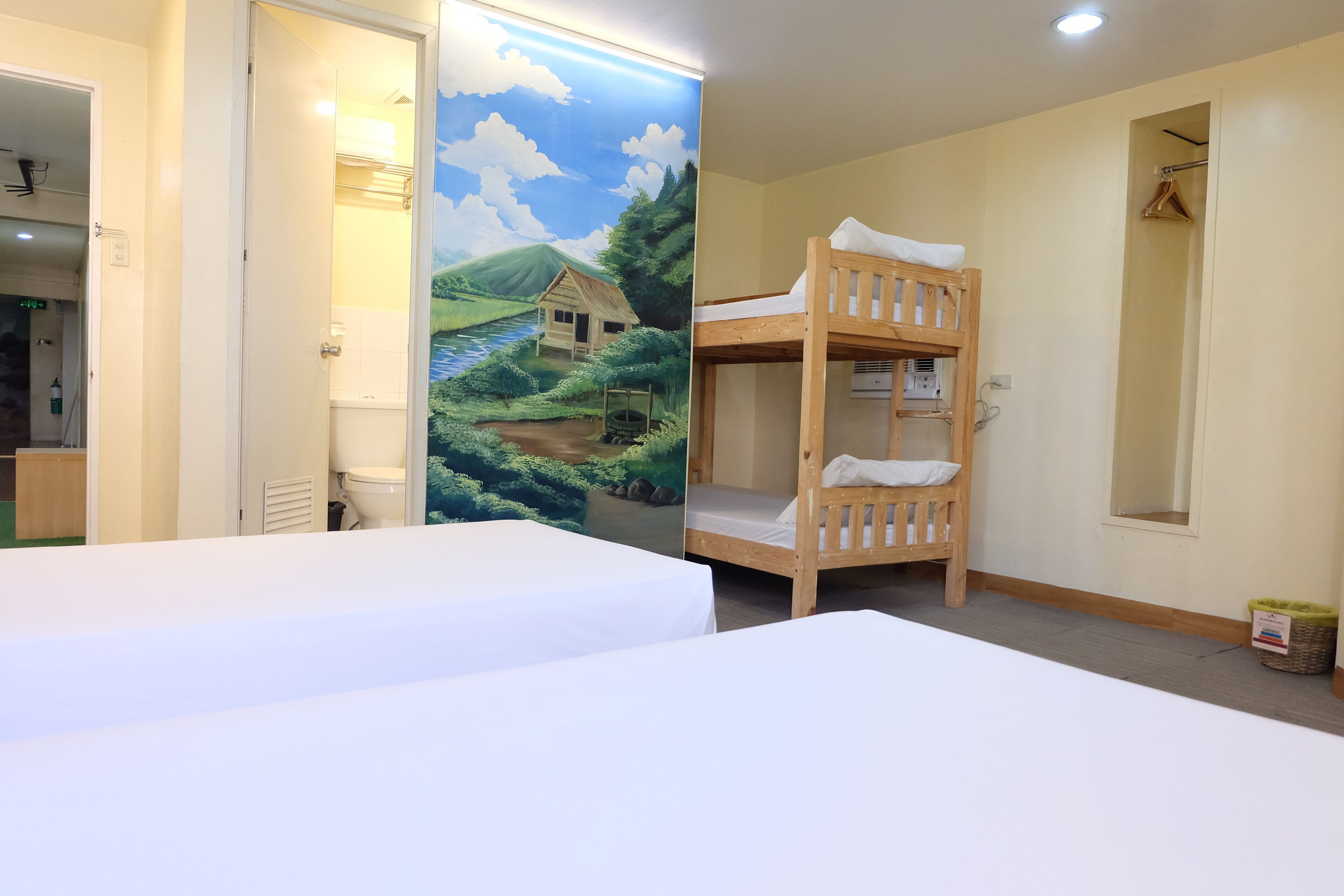 Ein Zimmer mit Etagenbetten, einem Wandbild eines Hauses an einem Fluss und einem kleinen Fenster.