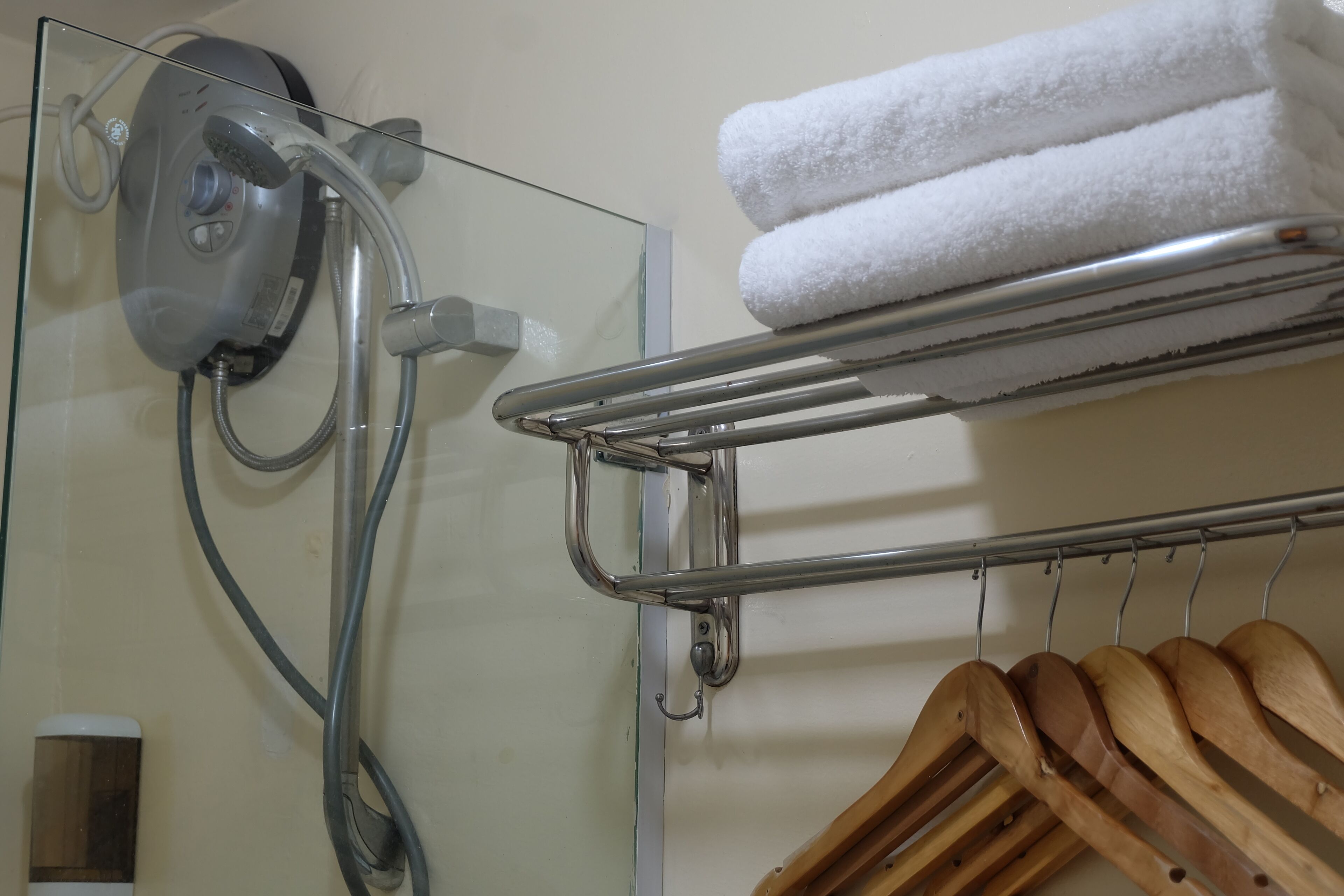 A glass shower enclosure with a handheld showerhead, a towel rack with folded towels, and a wooden hanger rack.