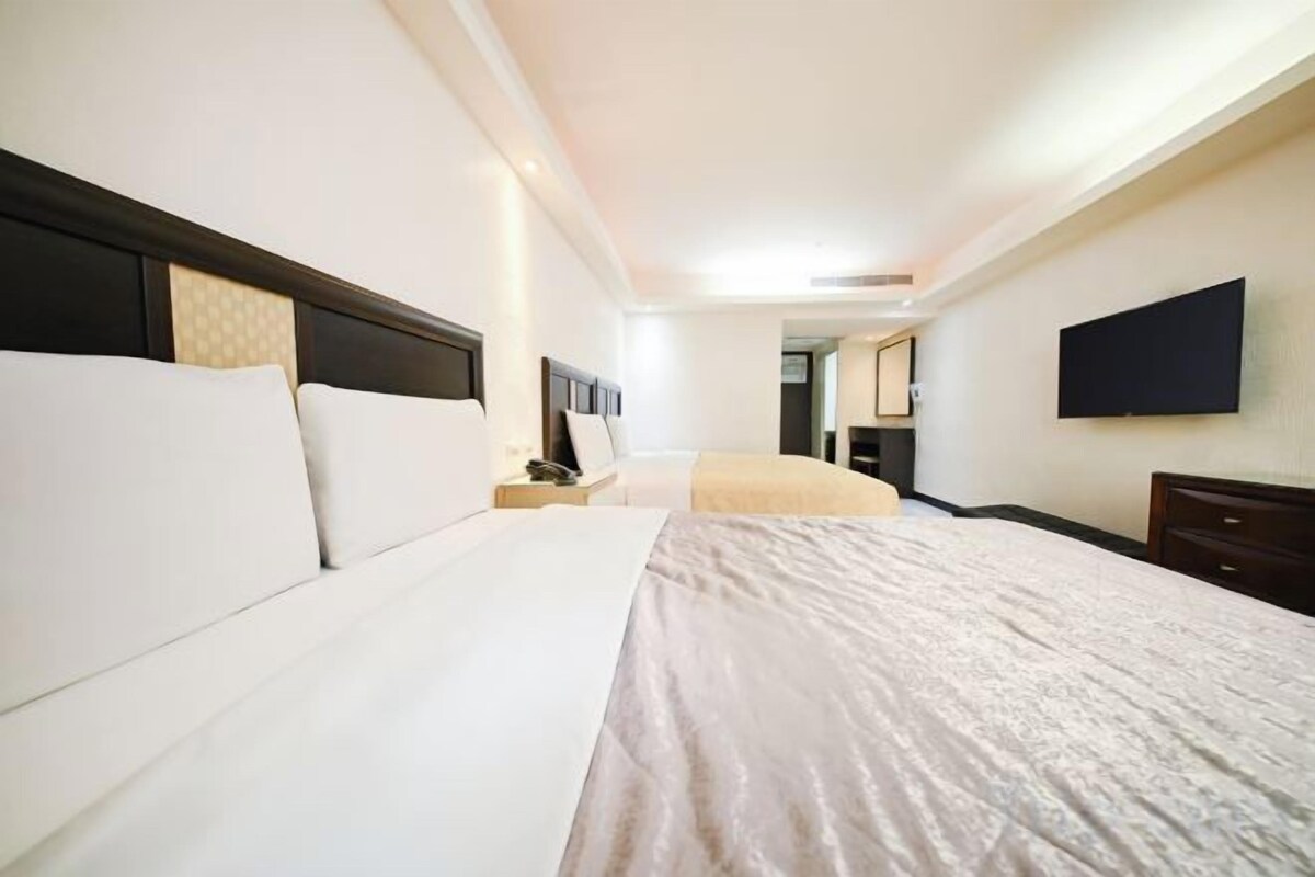 A hotel room with a large bed, bedside tables, a flat-screen TV, and a mirror on the wall.