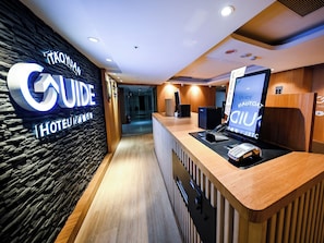 Een hotel receptie met een stenen muur, een receptiebalie, een digitaal scherm en een bord waarop 'TAOYANAN HOTEL' staat.