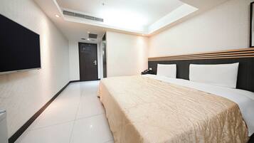 A hotel room with a bed, a flat-screen TV, a desk with a phone, and a door with a digital display.