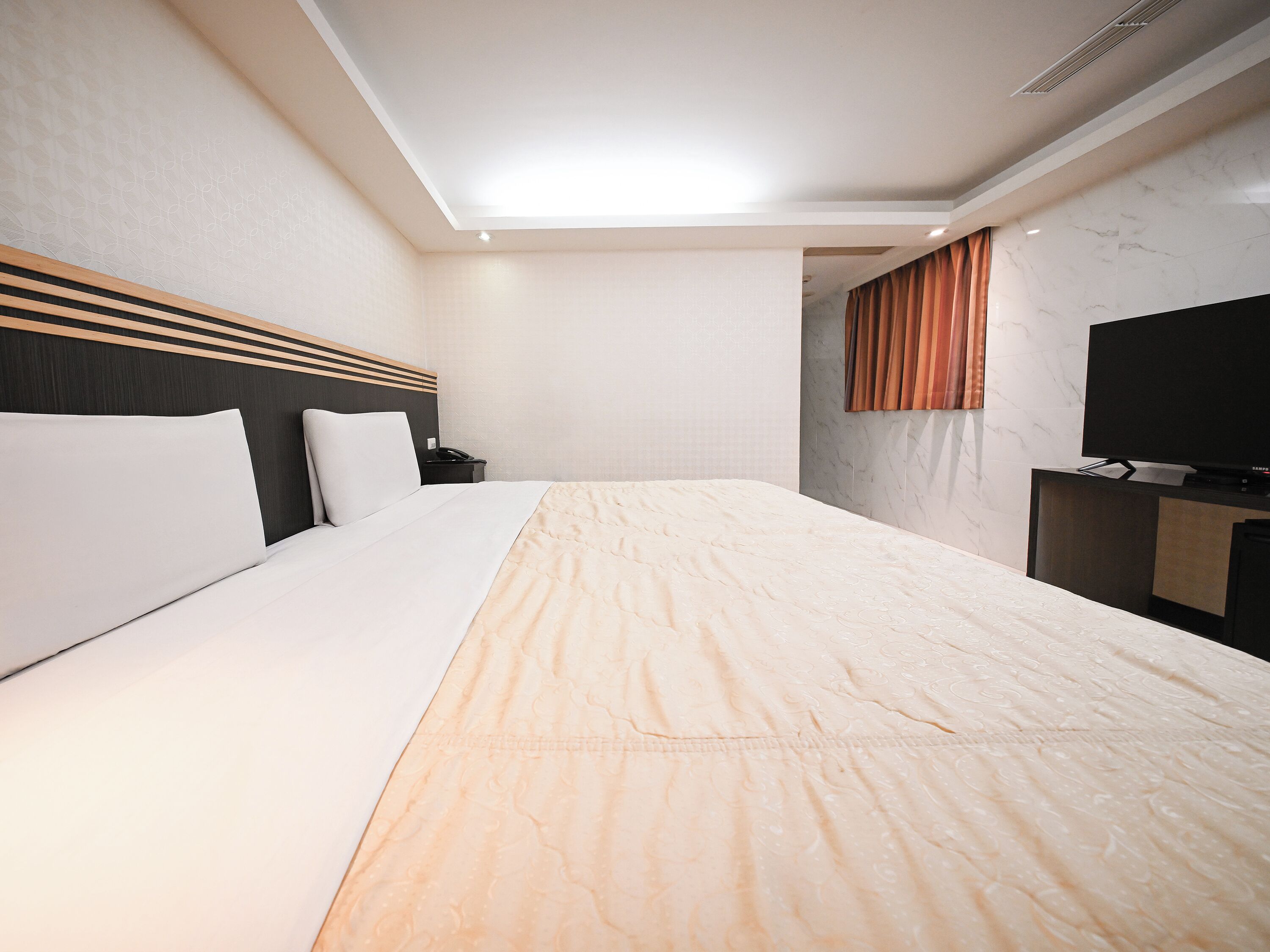 A hotel room with a bed, a TV, a desk, and a bathroom visible through a door.
