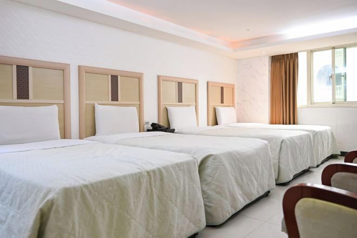 A hotel room with two beds, a desk, and a window with curtains.