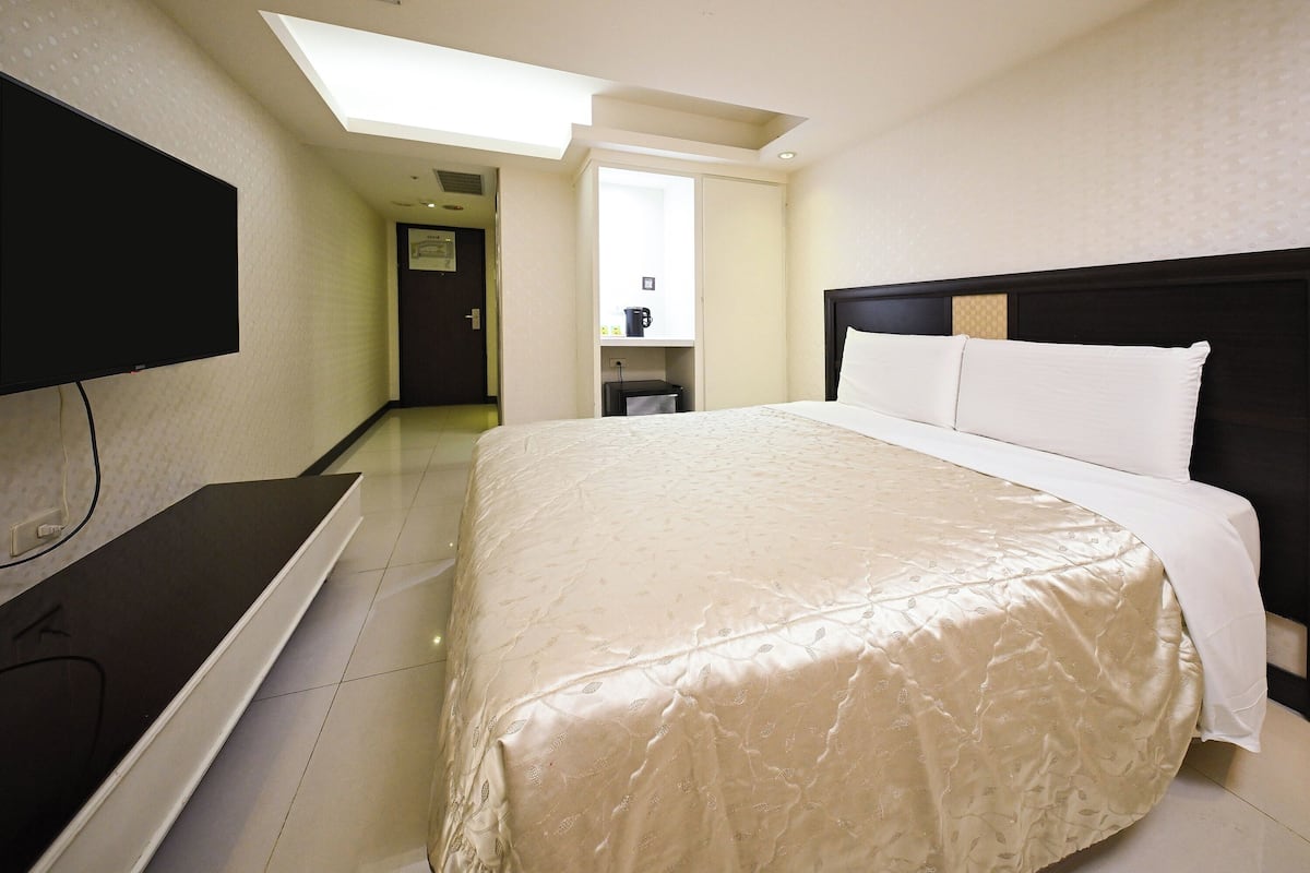 A hotel room with a bed, a television, a desk, and a bathroom visible in the background.