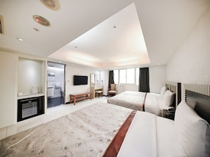 Een hotelkamer met twee bedden, een televisie, een bureau met stoel, een bankje en een raam.