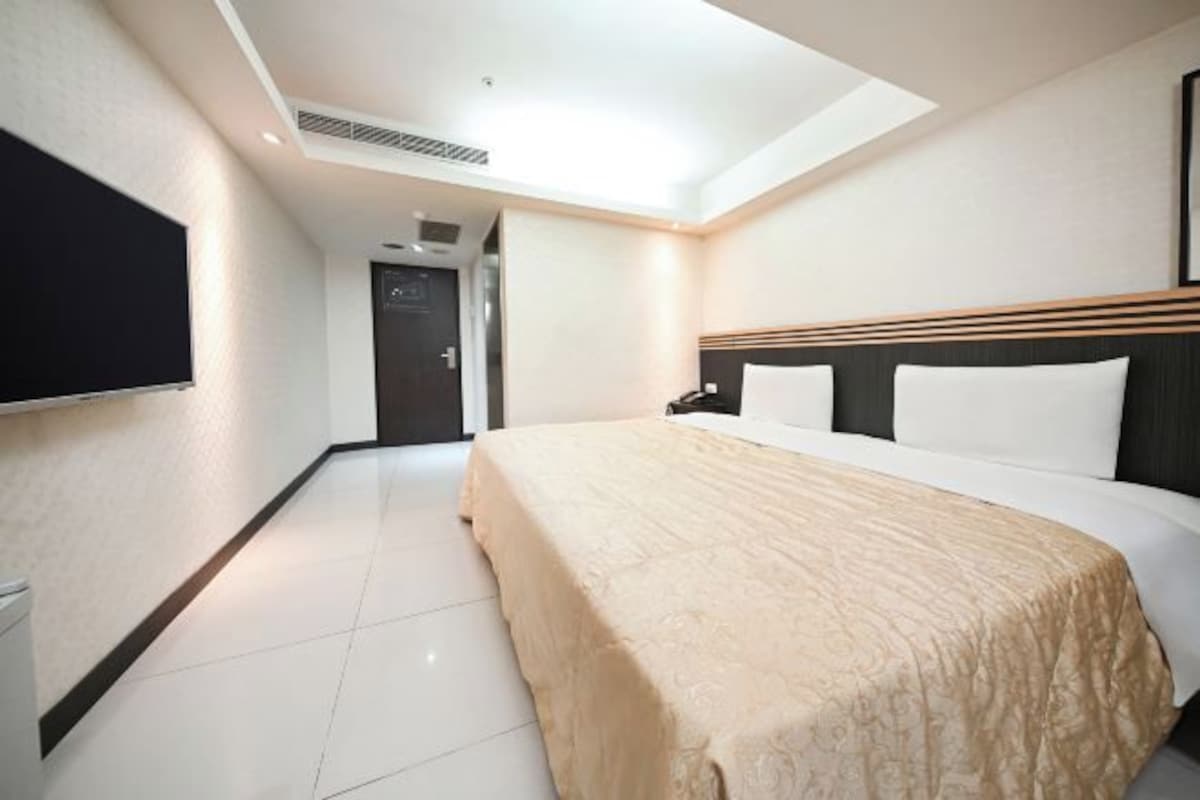 A hotel room with a large bed, a flat-screen TV mounted on the wall, and a door leading to another room.