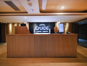 A hotel reception desk with a digital screen displaying 'TAOYUAN GUIDE HOTEL' and a phone.