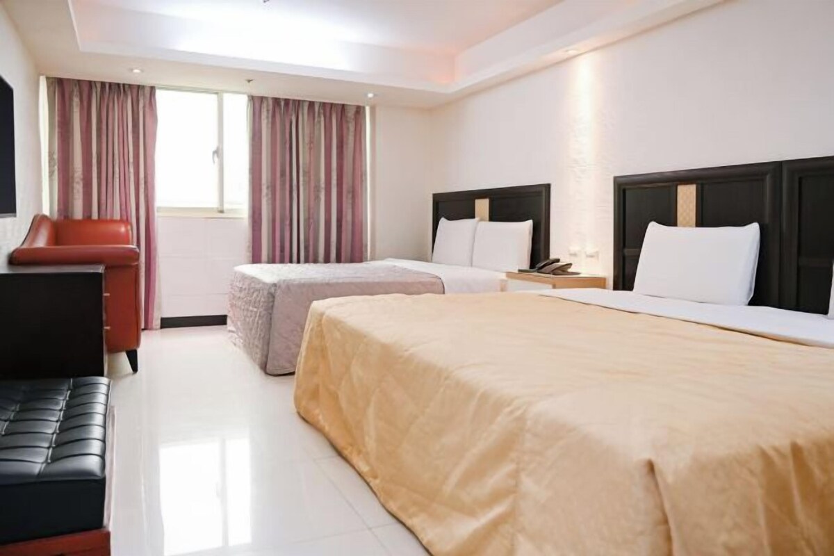 A hotel room with two beds, a desk, a chair, and a window with curtains.