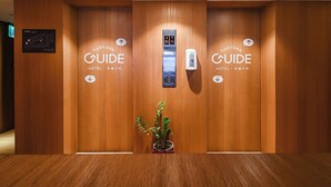 Et hotellets reception med træpaneler, et digitalt elevatordisplay og en stueplante.