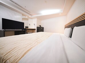 Ein Hotelzimmer mit einem großen Bett, einem Flachbildfernseher, einem Schreibtisch mit Stuhl und einem Kleiderschrank.