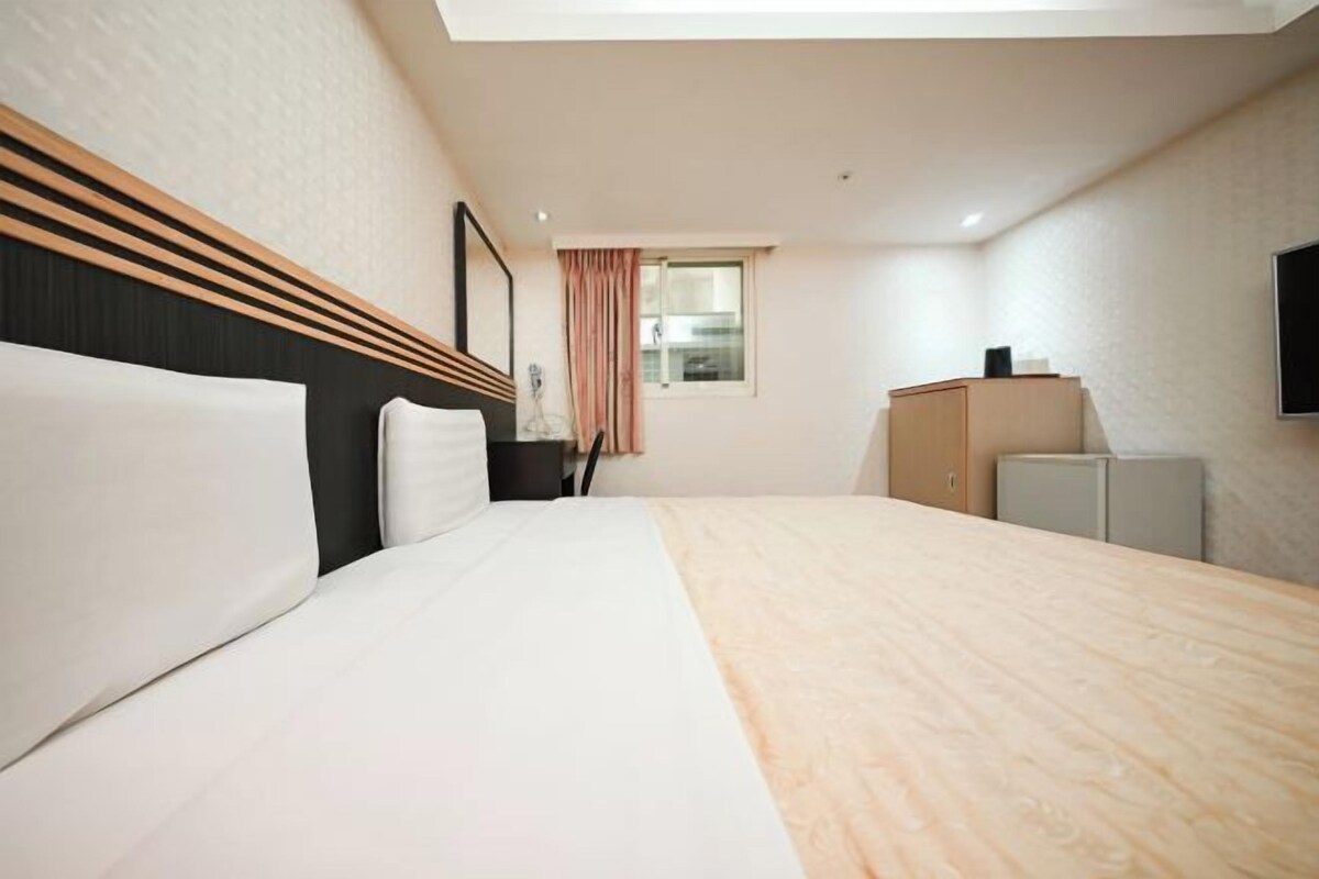 A hotel room with a large bed, a desk, a wardrobe, a TV, and a window with curtains.