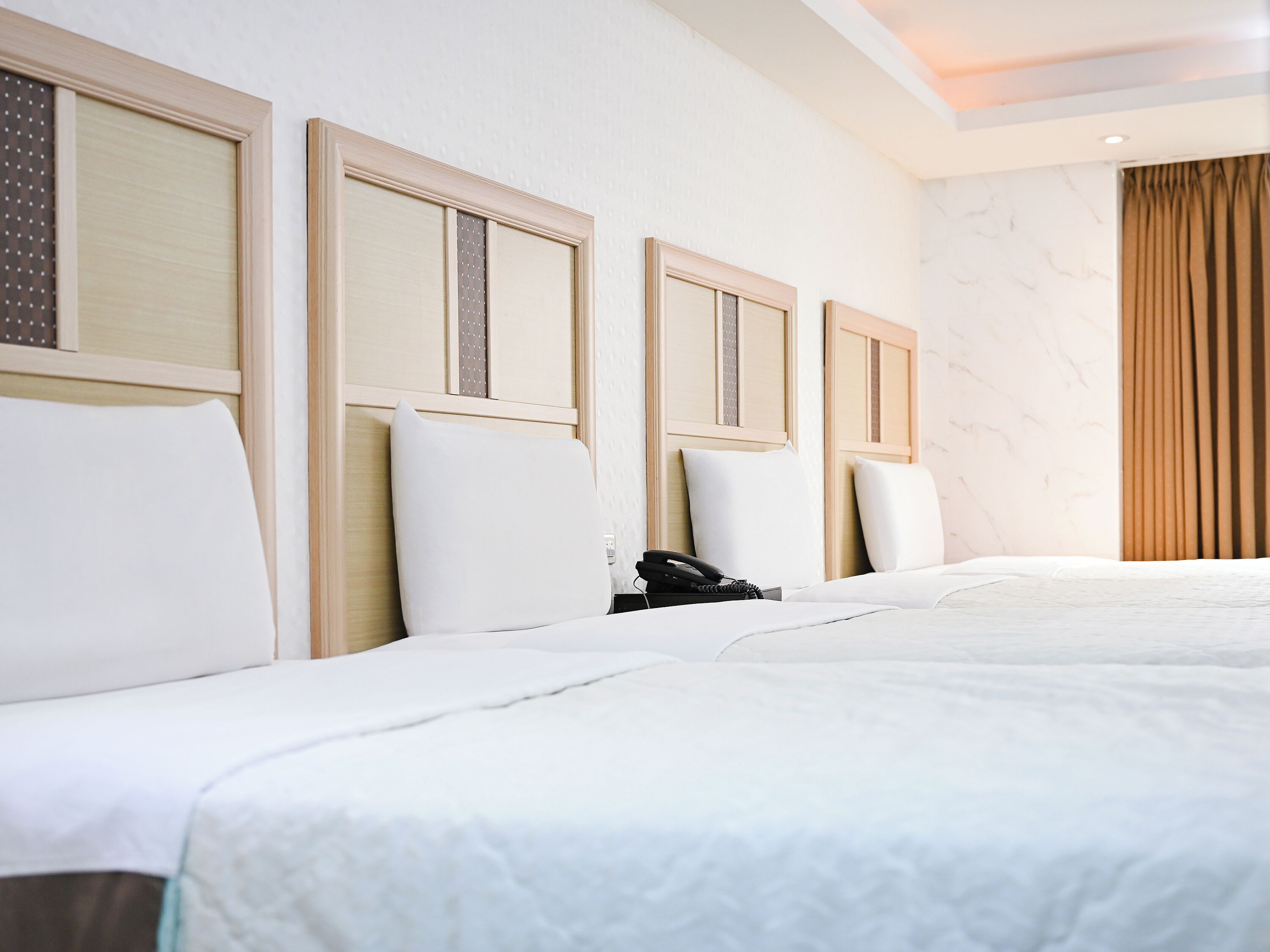 A hotel room with a large bed, a telephone, and a wall with a curtain.