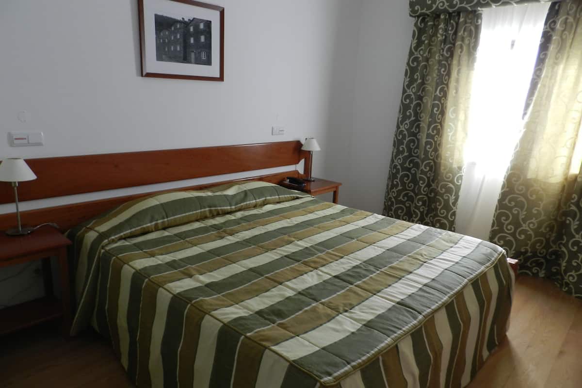 A hotel room with a bed, a nightstand, a lamp, a framed picture on the wall, and curtains.