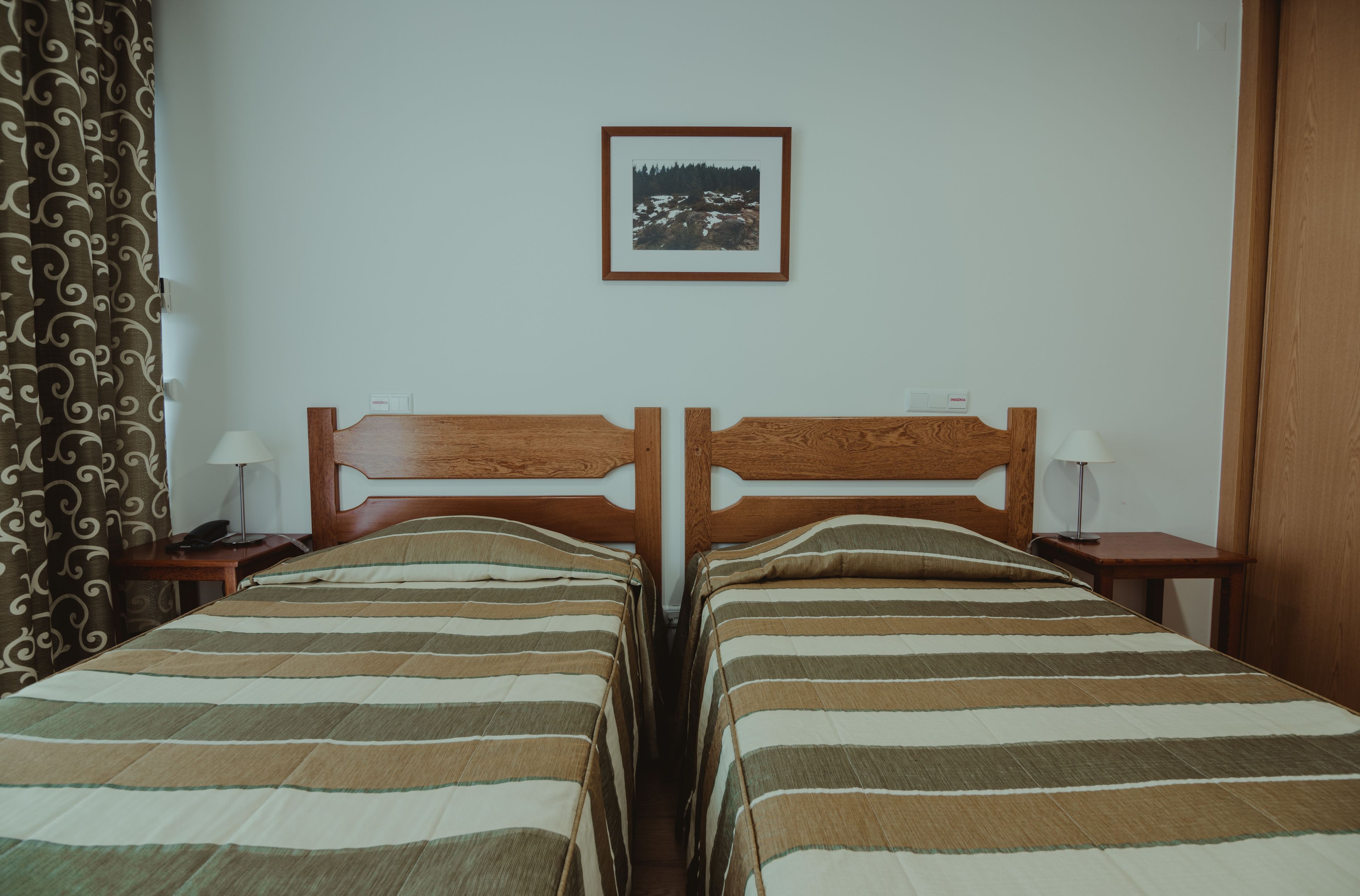 A double room with two beds, a framed picture on the wall, and a curtain on the left.