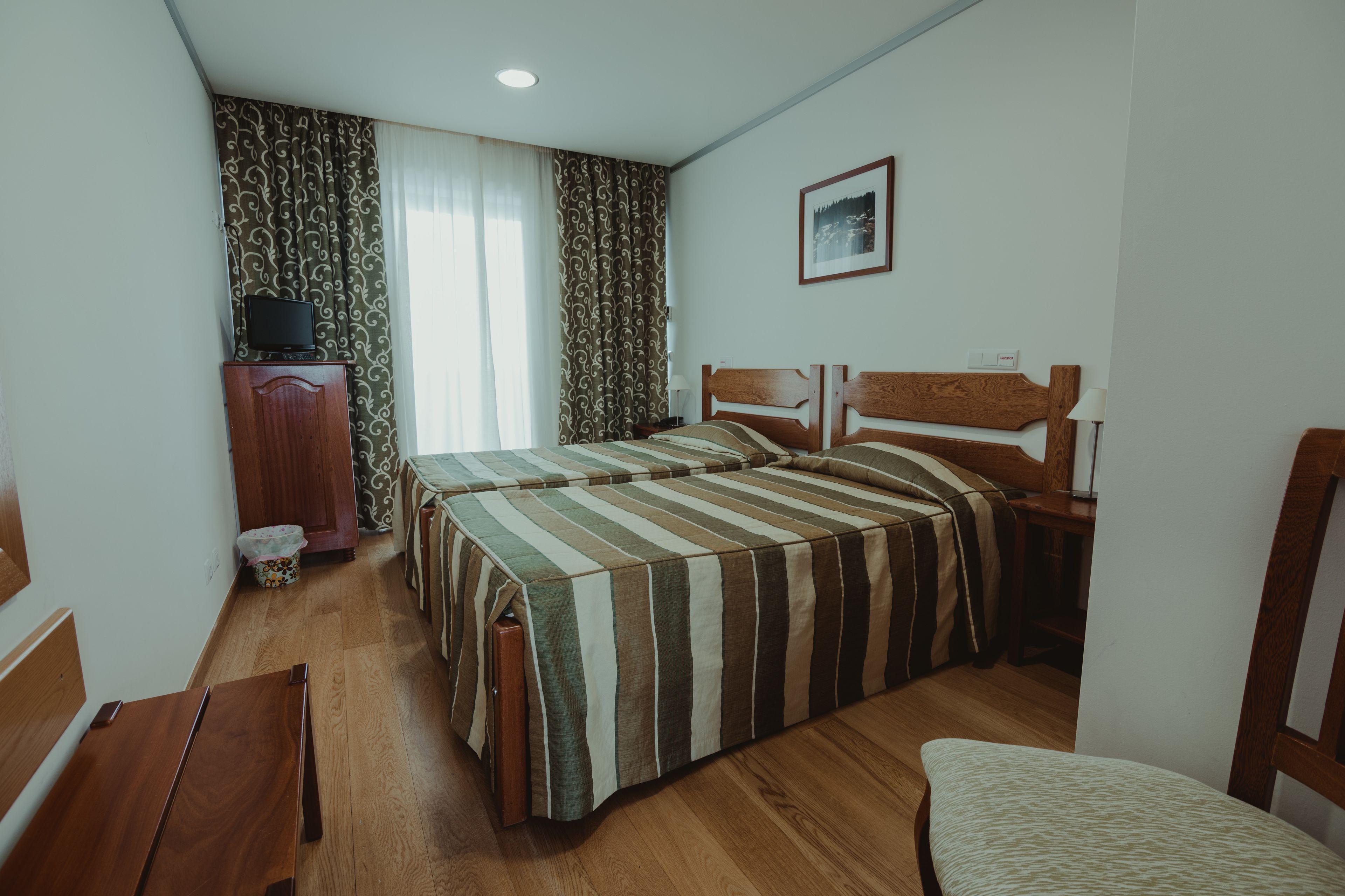 Una habitación de hotel con dos camas, muebles de madera, un televisor sobre un mueble bajo y una ventana con cortinas.