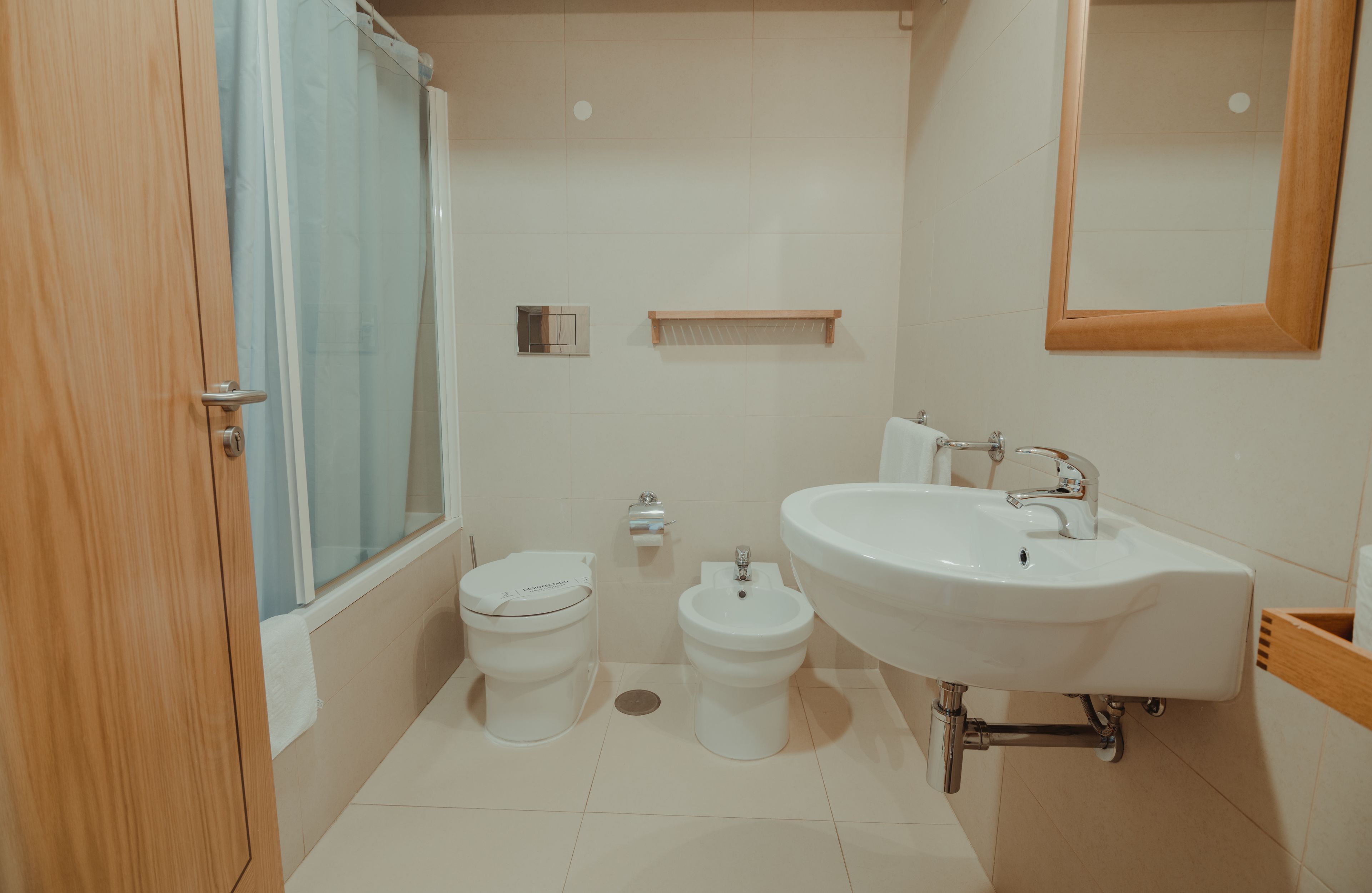 Un baño con inodoro, bidé, lavamanos, espejo y cortina de ducha.
